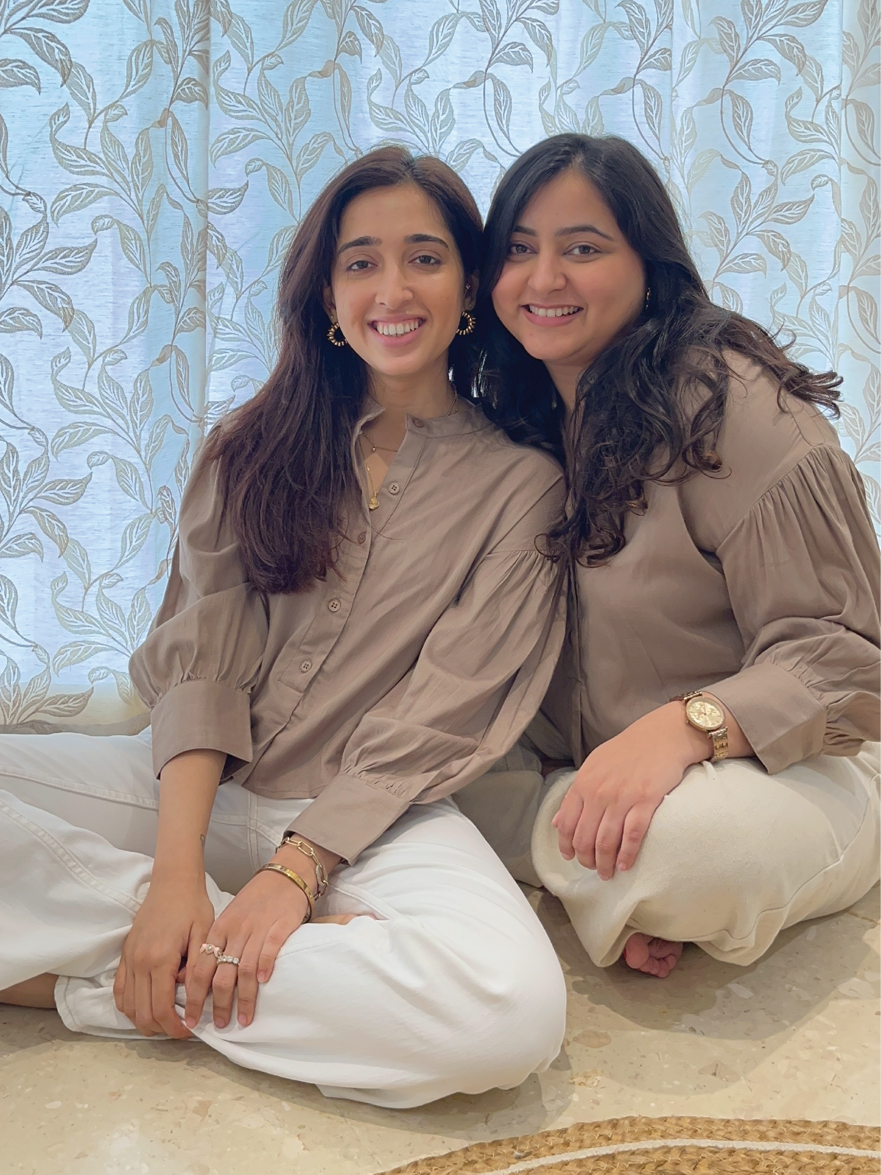 Two women sitting together against a decorative wall wearing Rerasa Cropped Band Collar Top