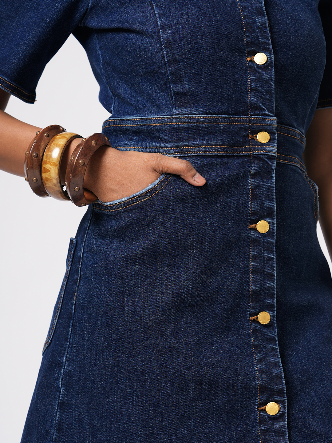 Close-up of a person wearing a blue Rerasa denim dress with gold buttons on a light gray background