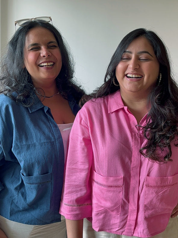 Two women standing side by side, one wearing a blue shirt and the other in pink, both smiling. Lace insert linen blend shirt