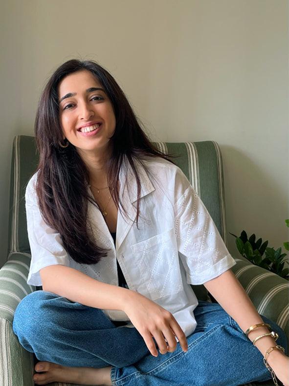 Woman sitting on a striped chair wearing a white shirt and blue jeans, smiling.